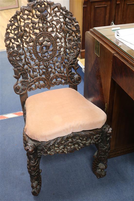 A Burmese carved hardwood low chair, having arched back and apron pierced with foliage, on lion dog and fish supports,